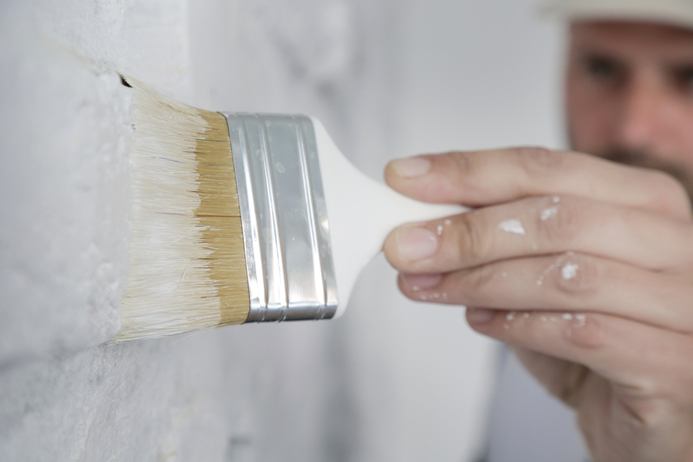 man painting white paint using brush onto the wall