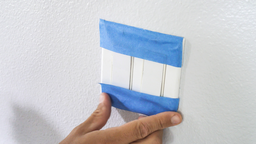 man putting blue masking tape at the edges of light switch
