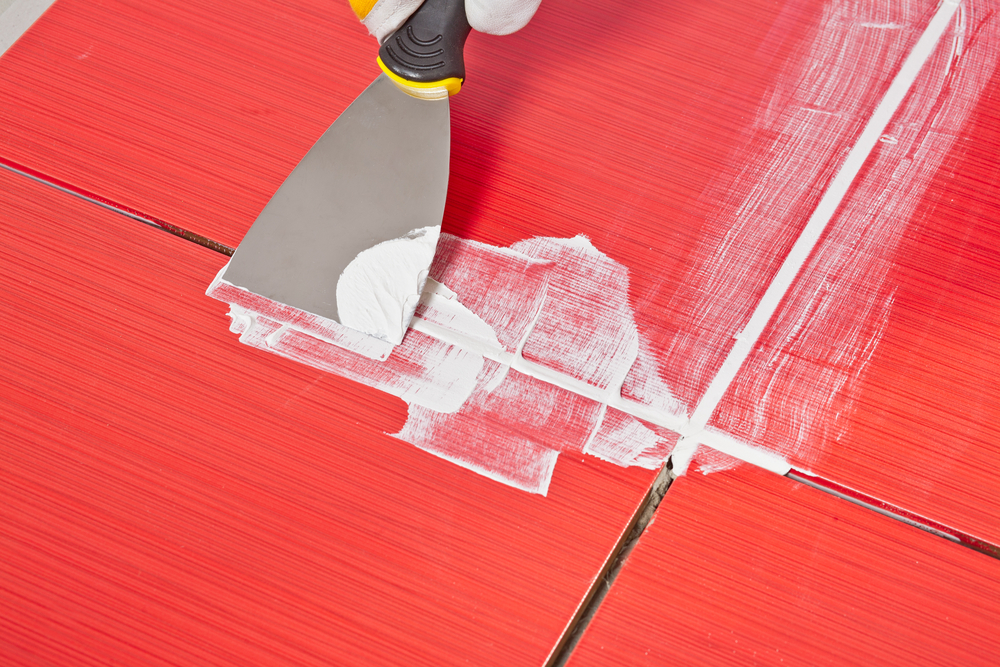 filling up grout between red ceramic tiles using filling knife