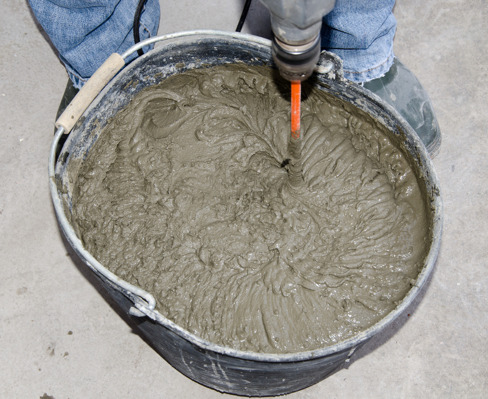 worker mixing powder adhesive with power drill in a bucket