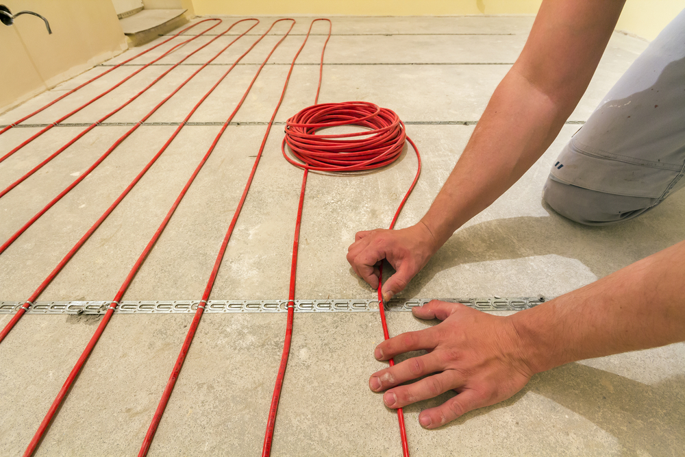 man installing heating red electrical cable wire on cement floor