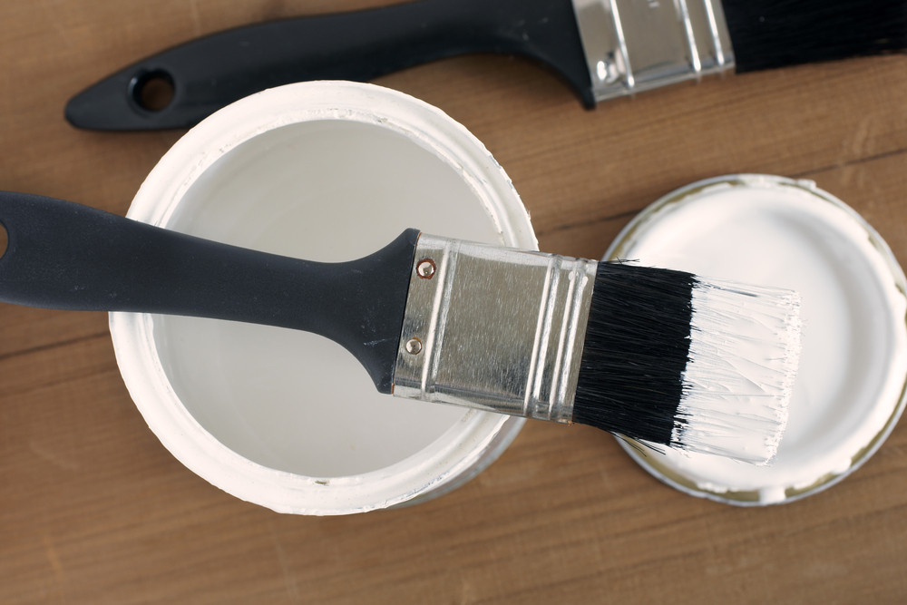 black paint brush above small can of white primer paint