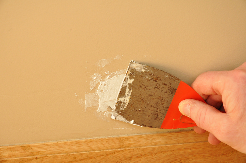 man using putty knife and wall filler to repair wall