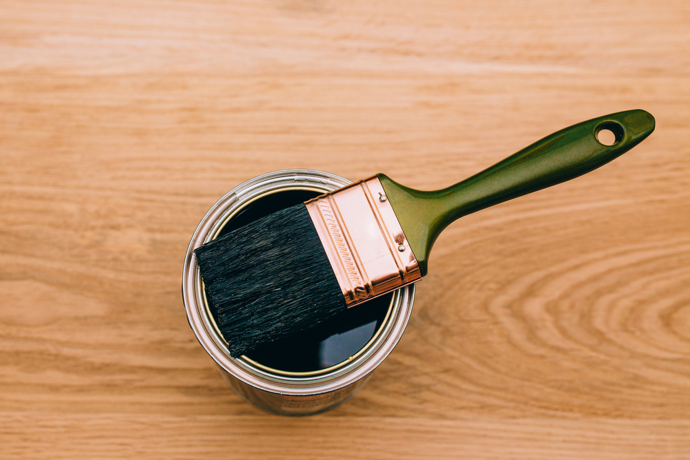 paintbrush above varnishing paint can