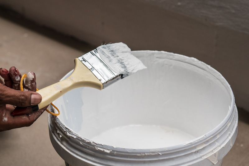 man holding paint brush over a bucket of white paint