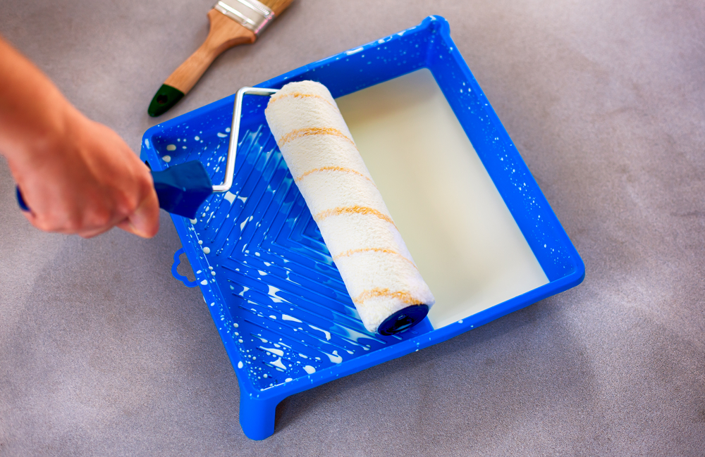 woman hand holding paint roller in blue paint tray that have white paint